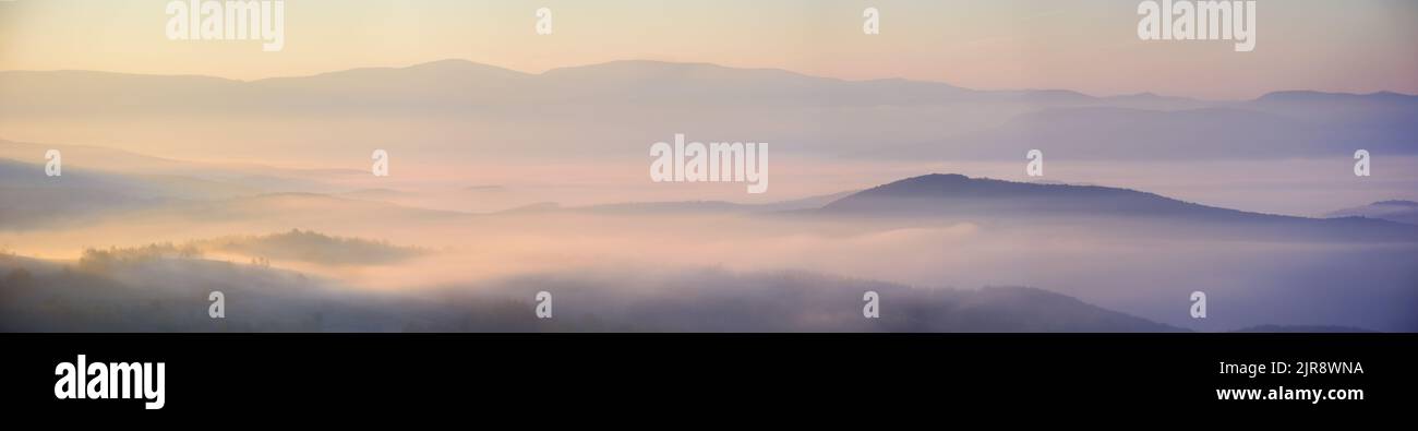 Bergige Landschaft bei Sonnenaufgang. Wolkeninversion im fernen Tal. Nebel zwischen den sanften Hügeln glühen im Morgenlicht. Wunderbar n Stockfoto