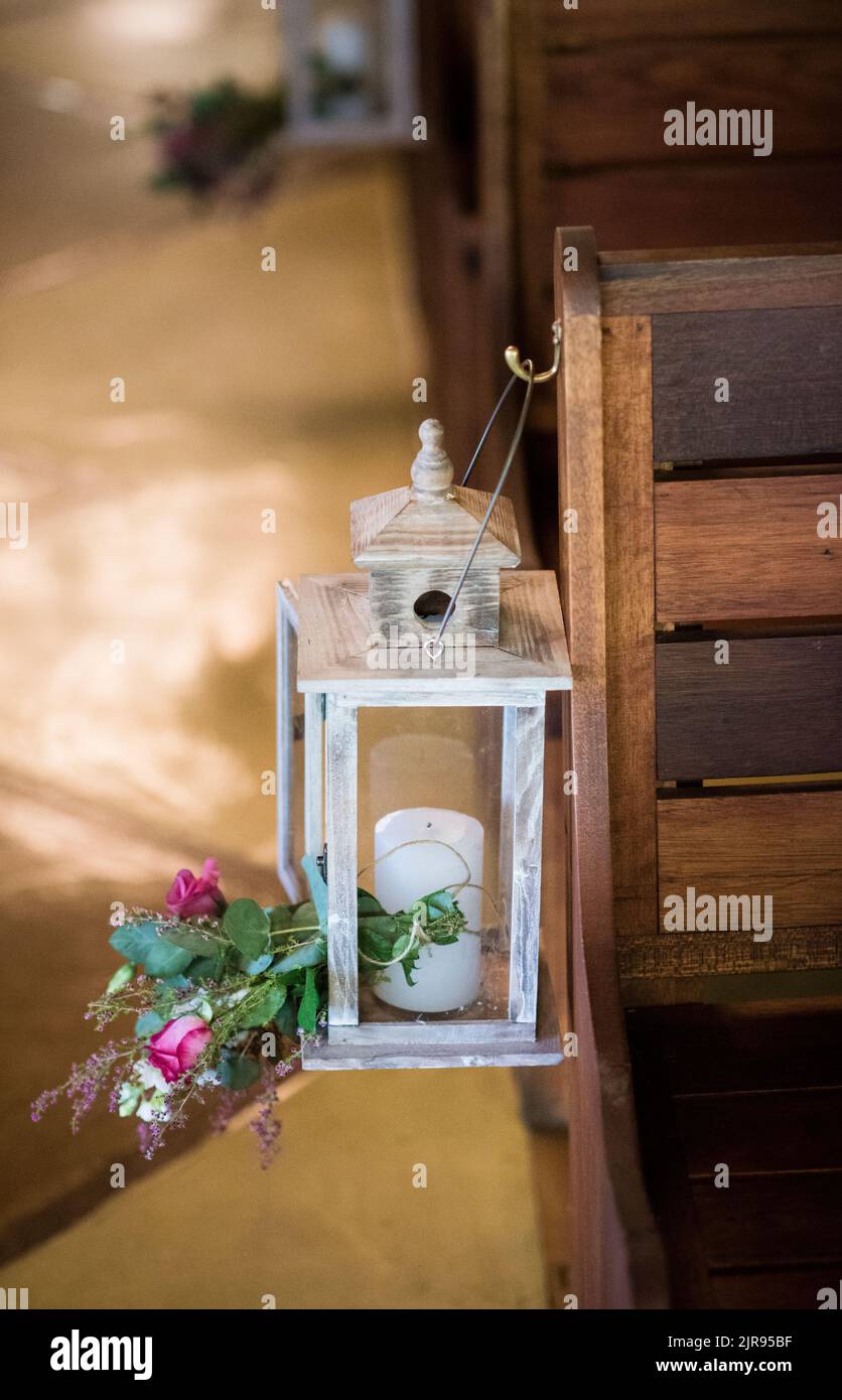 Eine vertikale Aufnahme einer Vintage-Lampe mit einer Kerze und Blumen, die auf einem Hochzeitssessel hängen Stockfoto