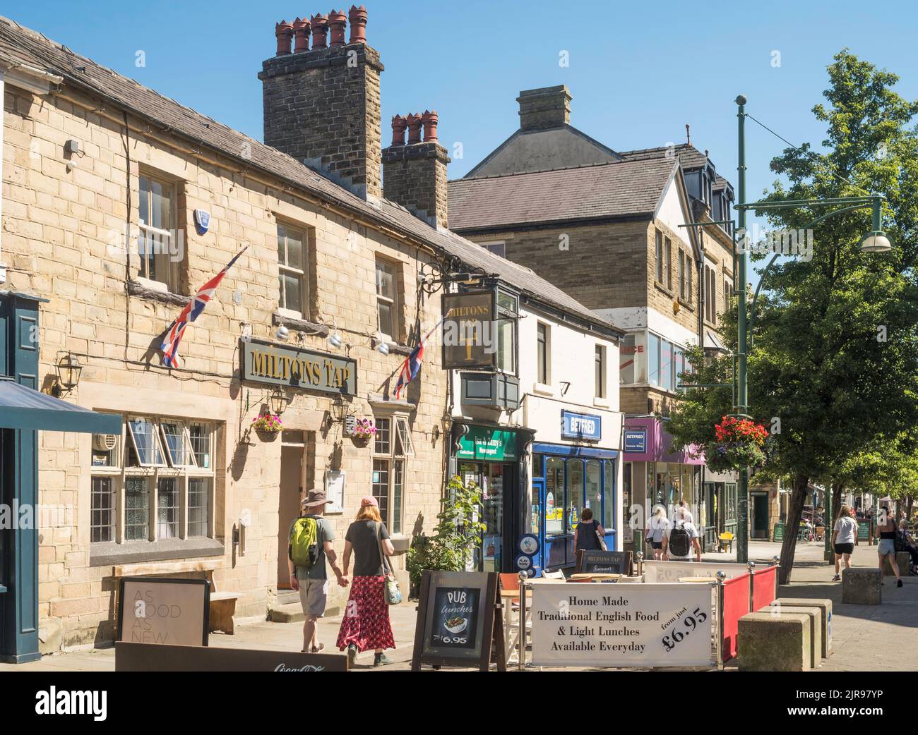 Ein Paar, das am Miltons Tap Pub im Stadtzentrum von Buxton, Derbyshire, England, Großbritannien, vorbeigeht Stockfoto