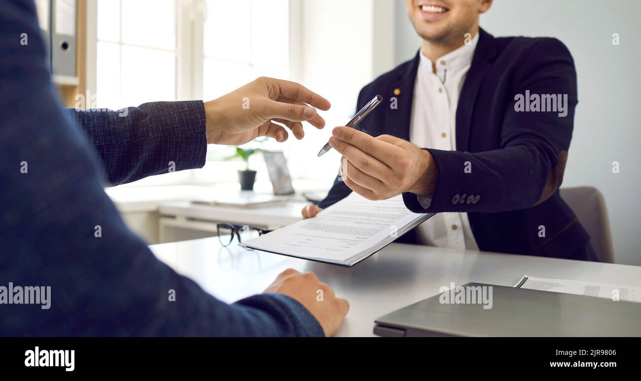 Der Agent übergibt einem Kunden einen Vertrag und einen Stift und bittet ihn, das Dokument zu unterzeichnen Stockfoto