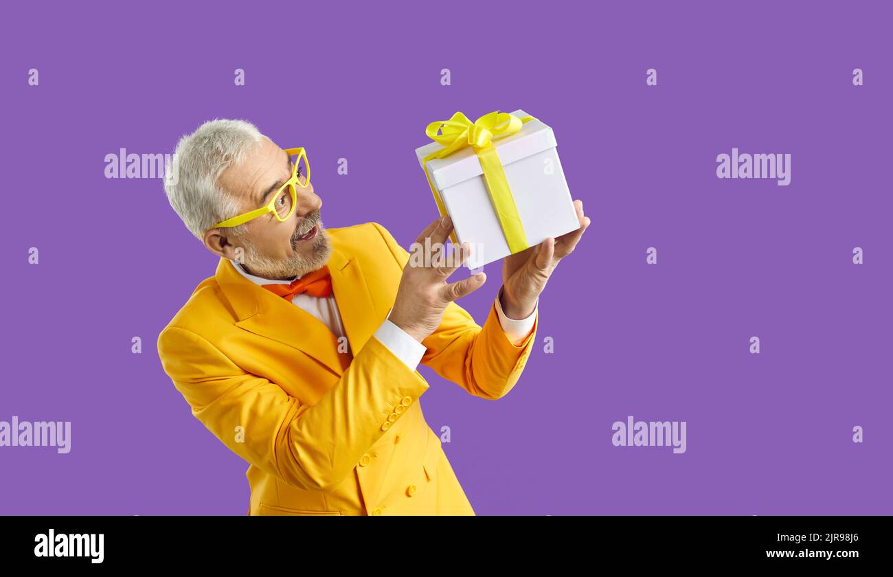 Lustig aufgeregt Senior Mann in Erstaunen genießt sein Geschenk isoliert auf lila Hintergrund. Stockfoto