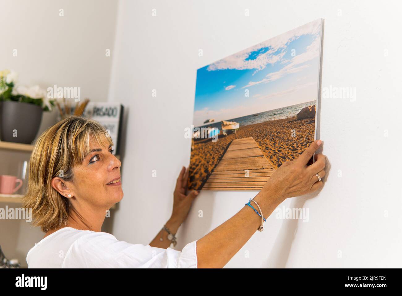 Frau zu Hause hängt ein Bild von einem schönen Strand in ihrem Wohnzimmer. Stockfoto