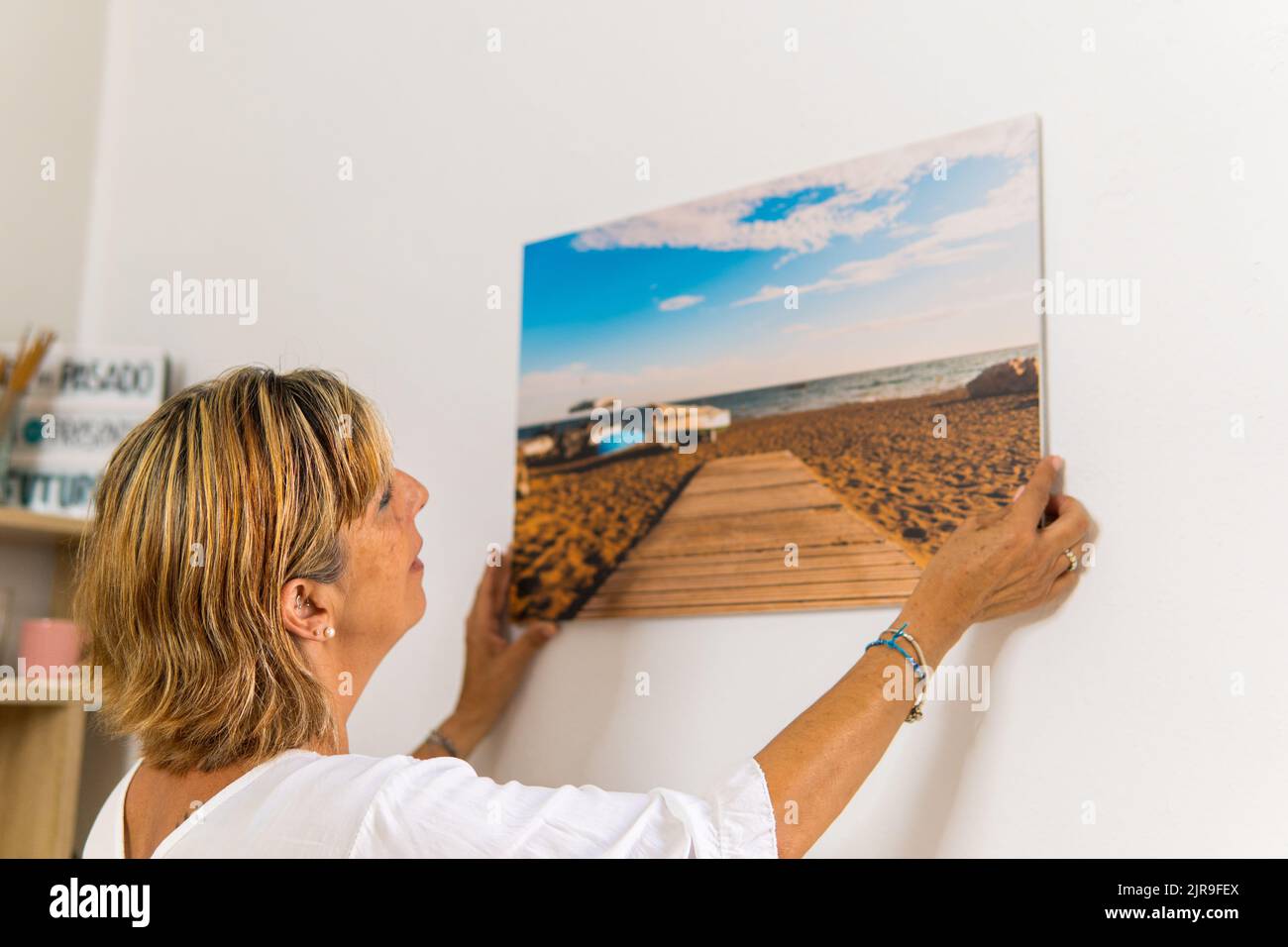 Erwachsene Frau, die ein sehr schönes Bild von einem Strand in Spanien aufgehängt hat. Stockfoto