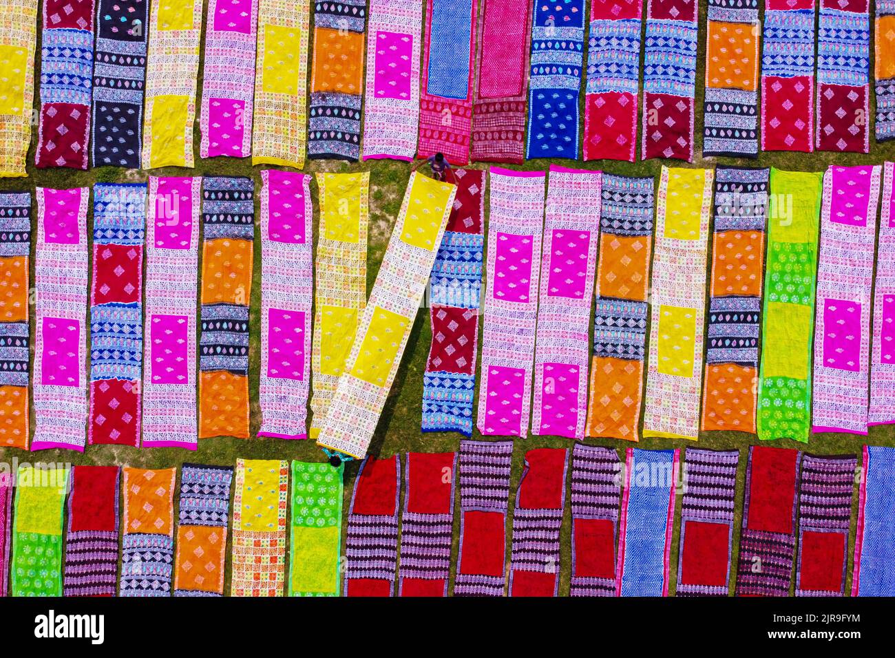 Narayanganj, Dhaka, Bangladesch. 23. August 2022. Farbenfrohe Stoffstreifen bilden ein auffälliges Display, da sie in ordentlichen Reihen auf einem Feld in Narayanganj, Bangladesch, angeordnet sind. Die langen Baumwolltücher werden lokal als ''Saree'' bezeichnet - ein traditionelles Kleidungsstück für Frauen, das unter der heißen Sonne trocknen soll und mit hellen Farben gefärbt wurde. Hier werden täglich etwa 4000 Stück Stoff zum Trocknen gelegt. Der Prozess dauert in der Regel drei Stunden, wobei jeder Satz von 200 Stück auf einmal bei Temperaturen trocknen kann, die über 36 Grad celsius erreichen können. Kredit: ZUMA Press, Inc./Alamy Live Nachrichten Stockfoto