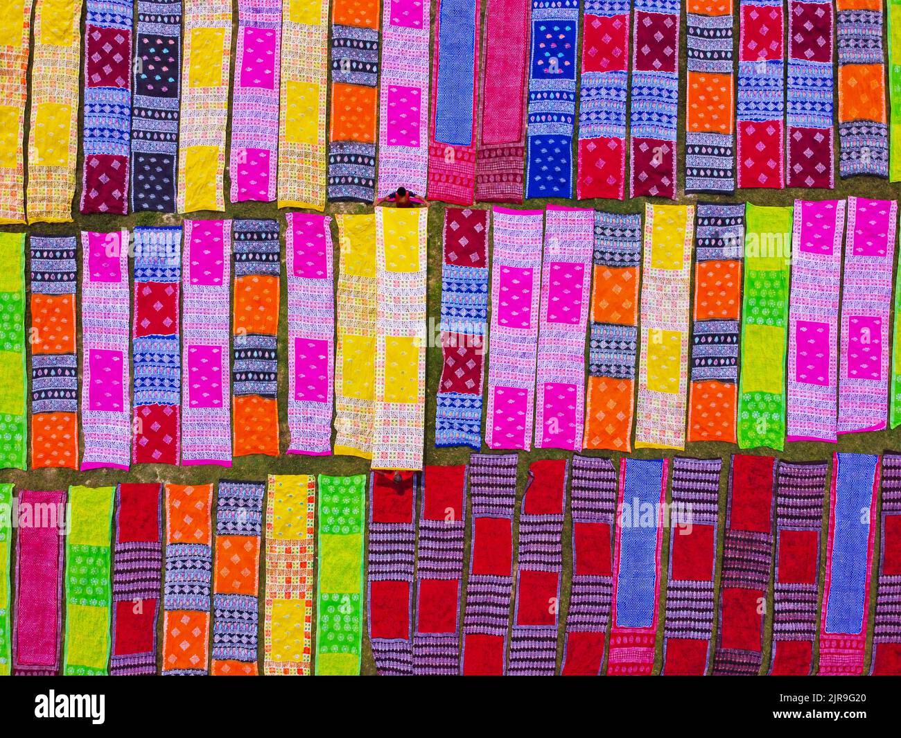 Narayanganj, Dhaka, Bangladesch. 23. August 2022. Farbenfrohe Stoffstreifen bilden ein auffälliges Display, da sie in ordentlichen Reihen auf einem Feld in Narayanganj, Bangladesch, angeordnet sind. Die langen Baumwolltücher werden lokal als ''Saree'' bezeichnet - ein traditionelles Kleidungsstück für Frauen, das unter der heißen Sonne trocknen soll und mit hellen Farben gefärbt wurde. Hier werden täglich etwa 4000 Stück Stoff zum Trocknen gelegt. Der Prozess dauert in der Regel drei Stunden, wobei jeder Satz von 200 Stück auf einmal bei Temperaturen trocknen kann, die über 36 Grad celsius erreichen können. Kredit: ZUMA Press, Inc./Alamy Live Nachrichten Stockfoto