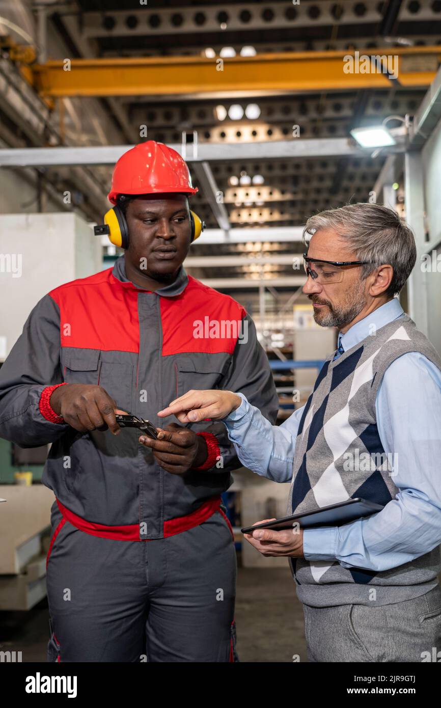 Multirassische Industrielle Mitarbeiter Stehen Und Reden Über Den Produktionsprozess. Schwarze Arbeiter Messen Mit Messschieber. Stockfoto