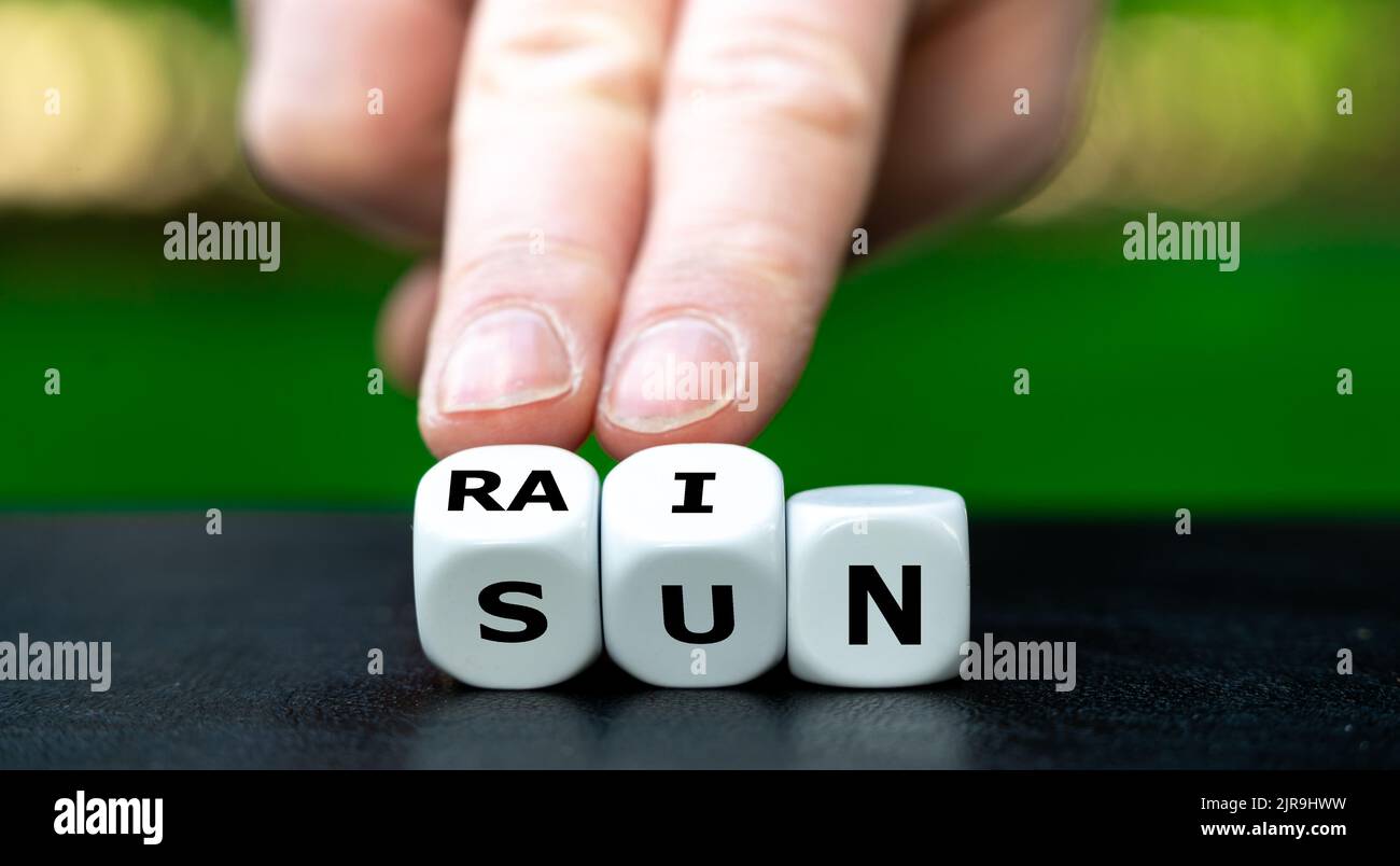 Die Hand dreht Würfel und ändert das Wort Sonne in Regen. Stockfoto