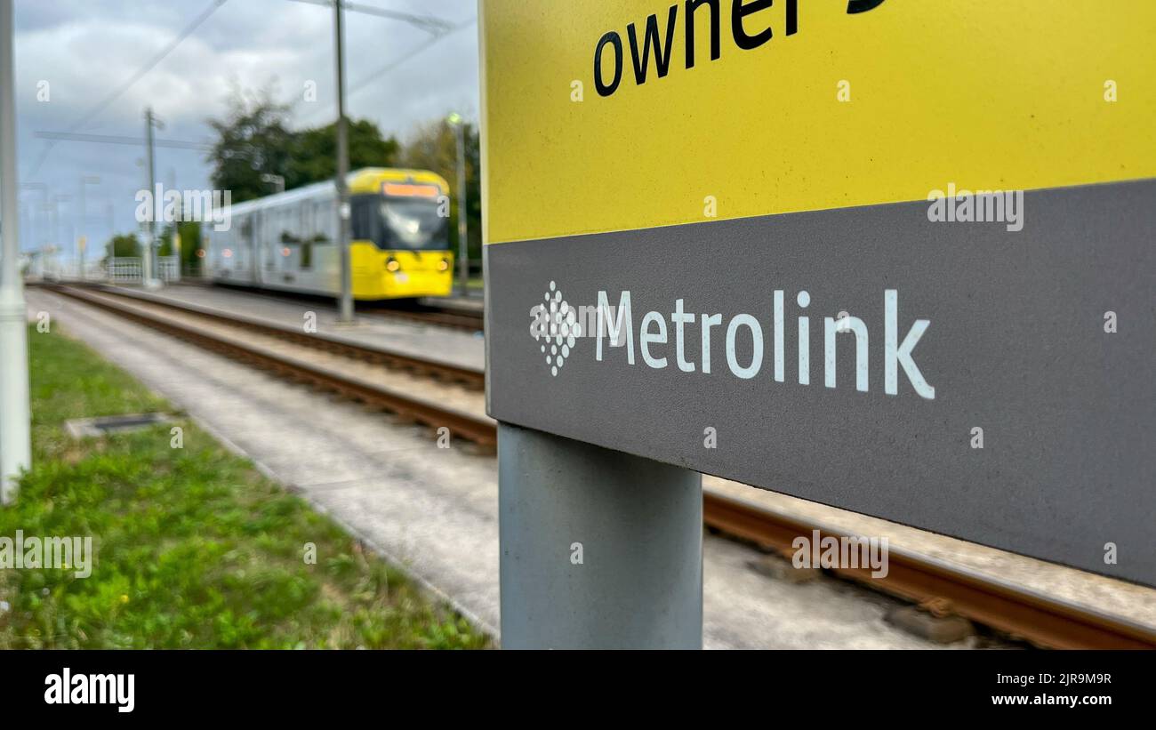 Ein Blick auf das Manchester Metrolnk Logo mit einer M5000 m langen Straßenbahn, die von der Haltestelle Martinscroft abfährt, ist unscharf Stockfoto