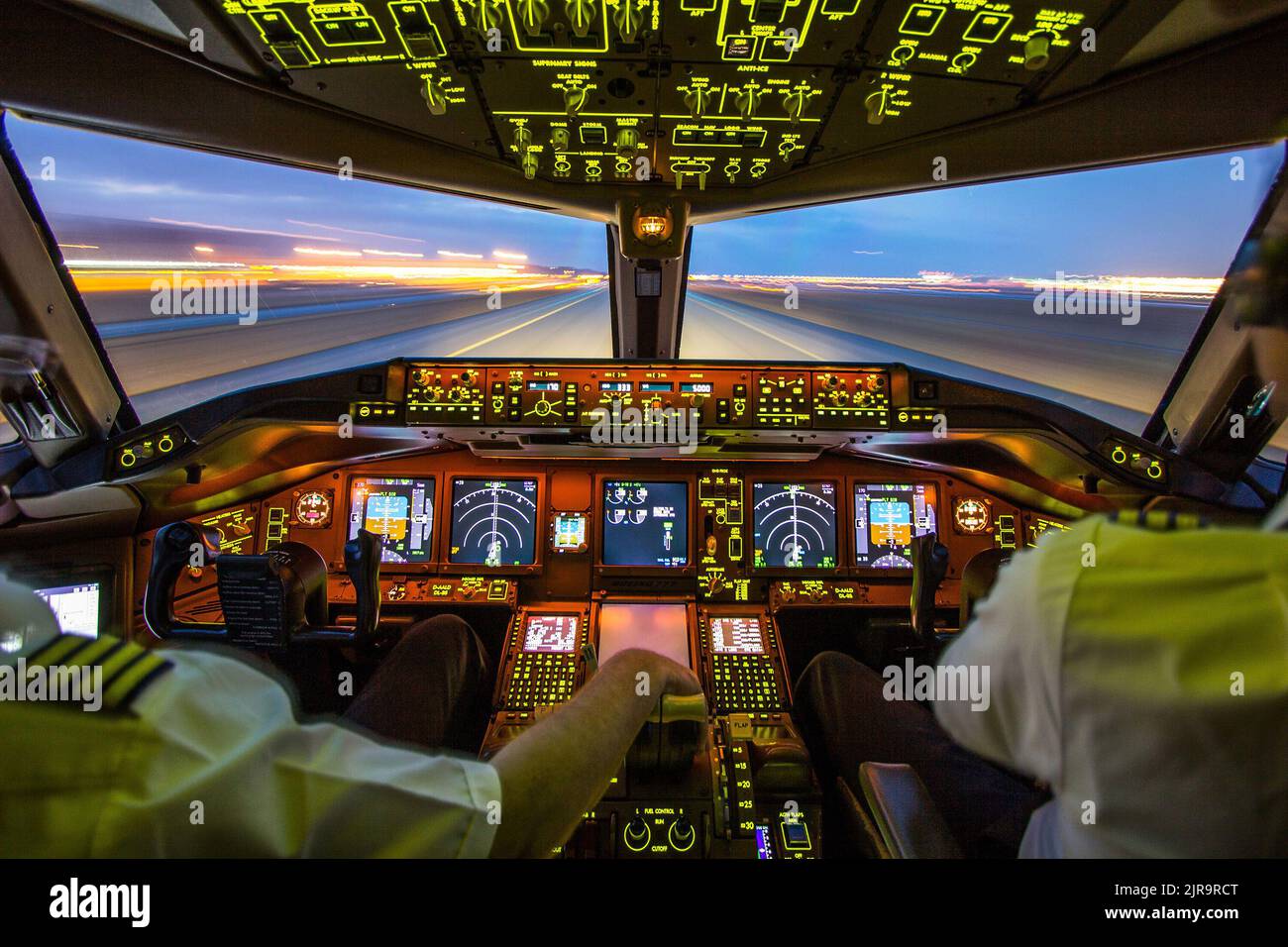 Airliner-Cockpit mit einem Piloten und einem Co-Piloten und einer Landebahn, die nachts vom Innenraum aus betrachtet wird Stockfoto