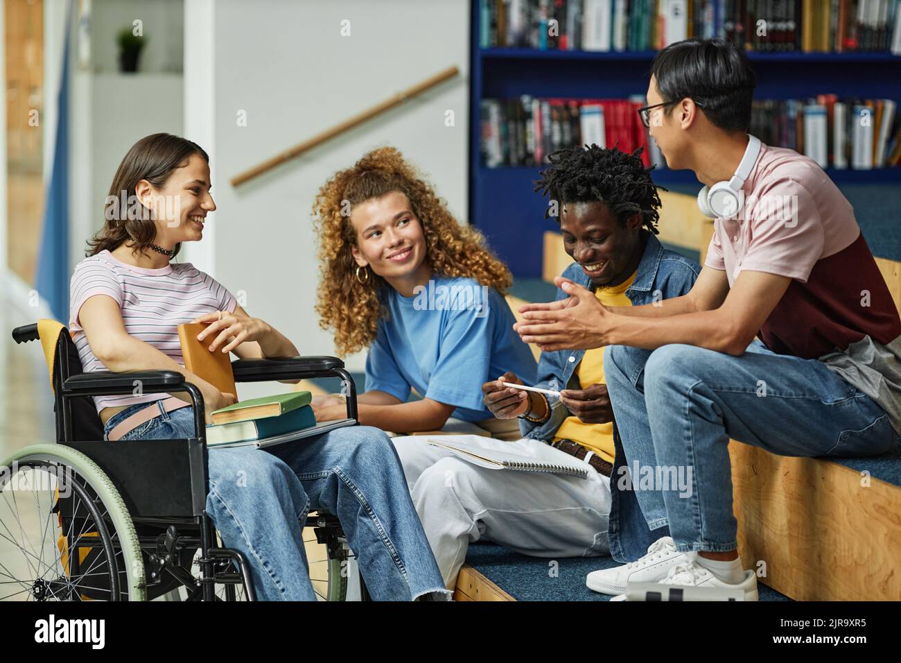 Eine vielfältige Gruppe junger Menschen, die in der Universitätsbibliothek plaudern, darunter auch eine Studentin mit Behinderung Stockfoto