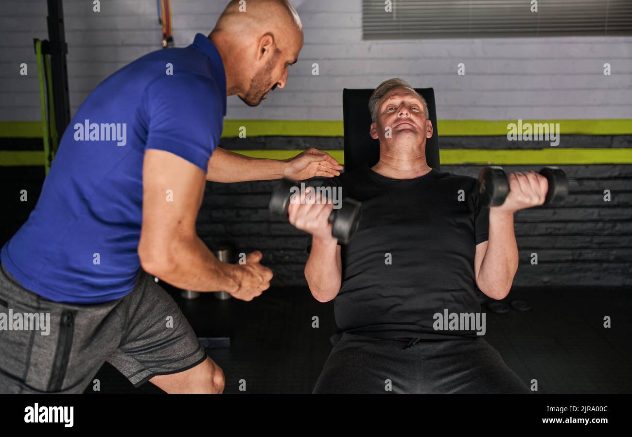 Reifer Mann und Personal Trainer tun gewichtete sitzende Arm Locken in der Garage Hausgymnastik Stockfoto