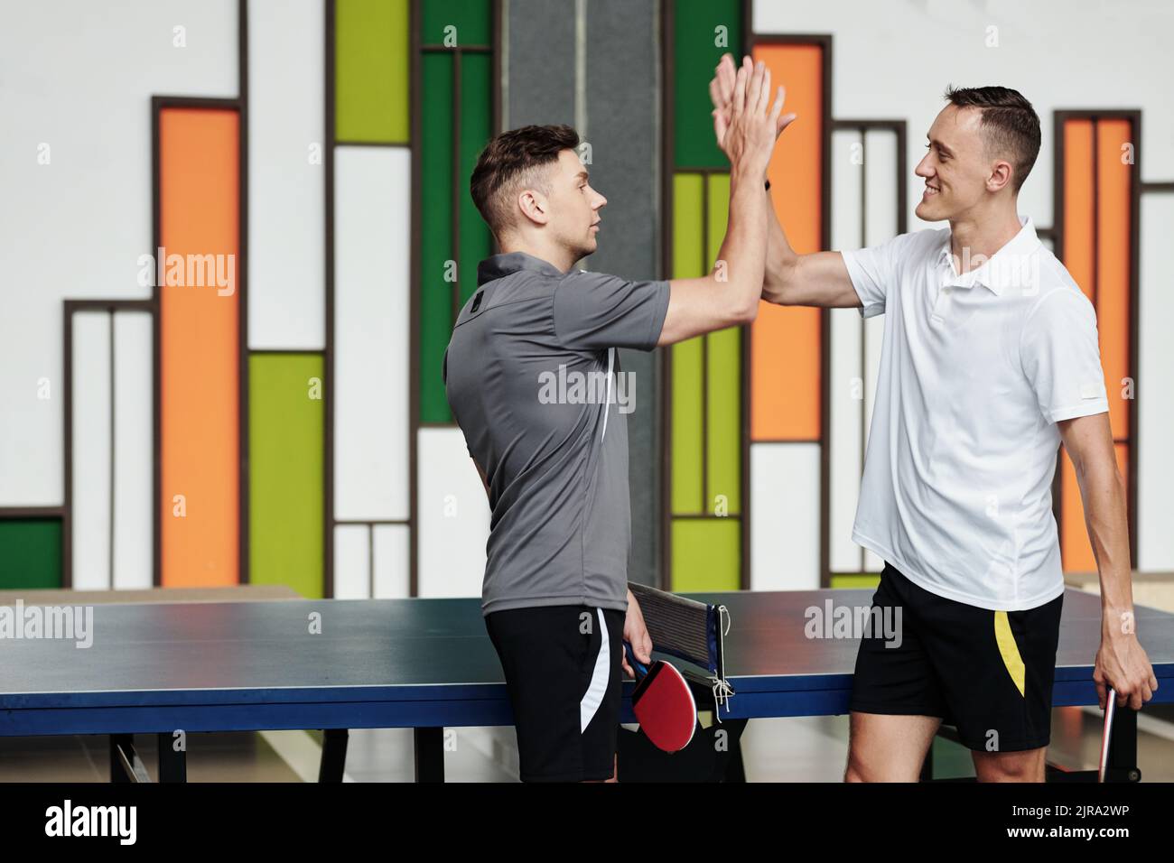 Positive junge Tischtennisspieler geben sich gegenseitig nach dem Spiel hohe fünf Stockfoto