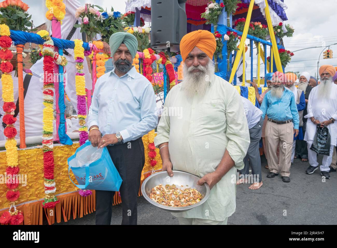 Während der Sikh Nagar Kirtan Parade bietet ein Marcher Zuschauern und Fotografen Nüsse an. An der Liberty Ave in richmond Hill, Queens, New York City. Stockfoto