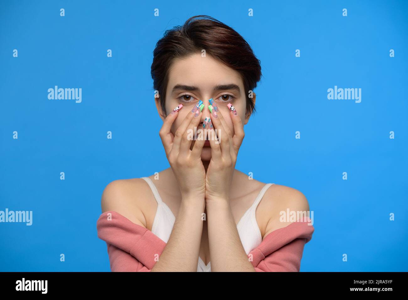 Skinny niedlichen Teenager-Mädchen versteckt Untergesicht in ihren Händen, blauer Hintergrund Stockfoto