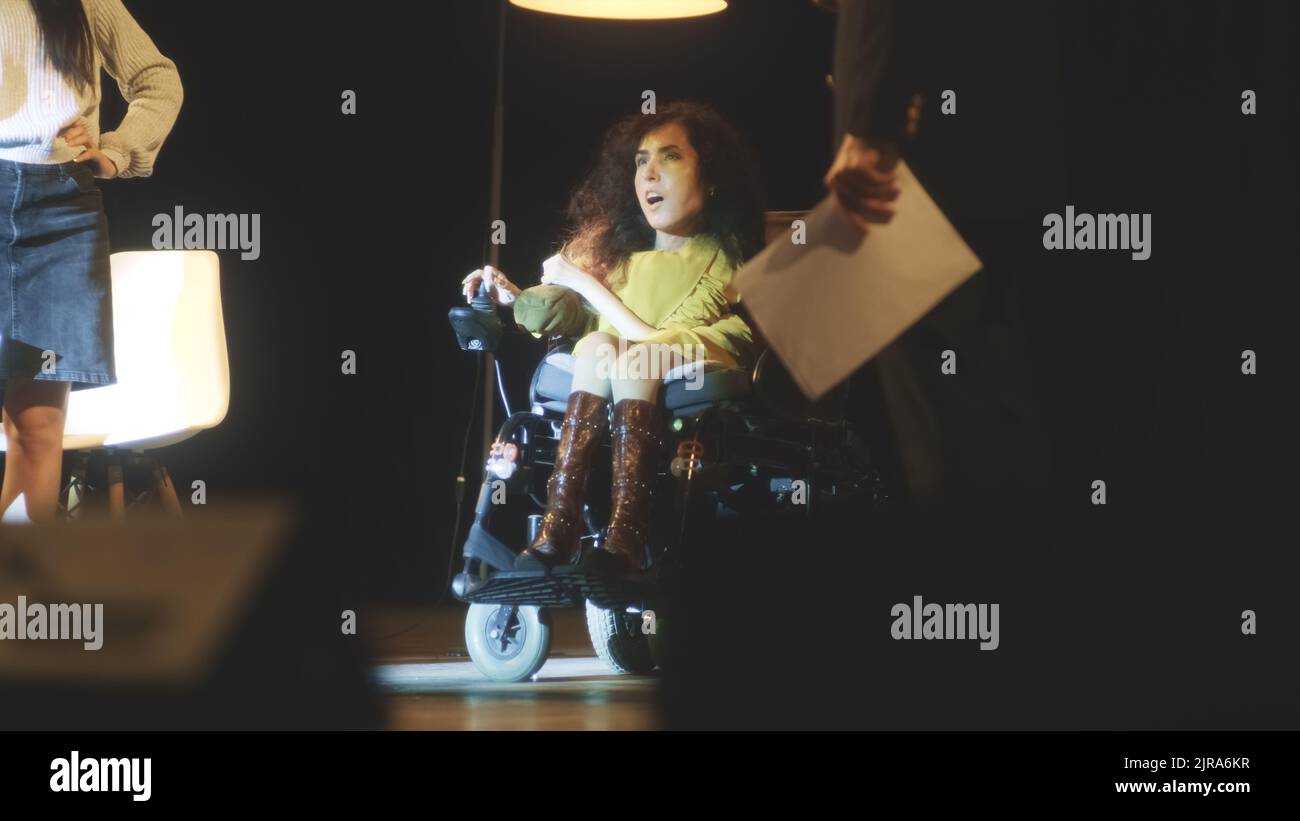 Schauspielerin mit einer Behinderung und anderen Schauspielern spielen zusammen eine Szene auf der Bühne mit Spotlight und Dekorationen im Theater während der Aufführungsprobe Stockfoto