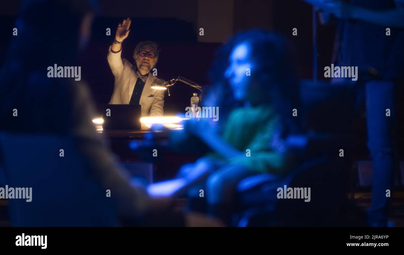 Eine behinderte Frau im Rollstuhl auf der Bühne mit Kollegen, die eine Rolle im Theater spielen und den Anweisungen des Regisseurs lauschen, während einer Aufführungsprobe Stockfoto