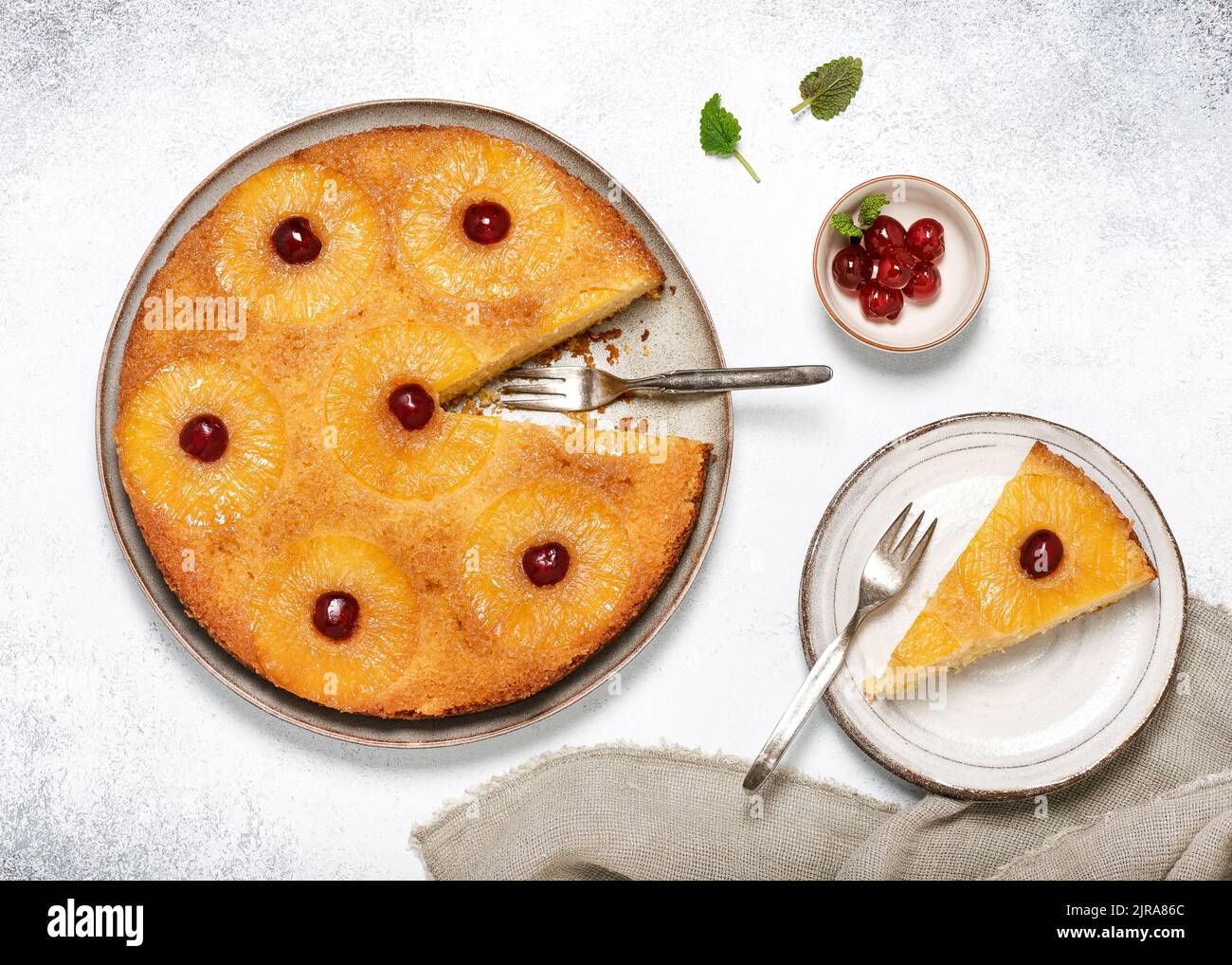 Draufsicht auf hausgemachten Ananas auf den Kopf gestellt Kuchen mit kandierten Kirschen und einem Stück abgeschnitten auf einem Teller. Tropisches Dessert im Sommer. Stockfoto