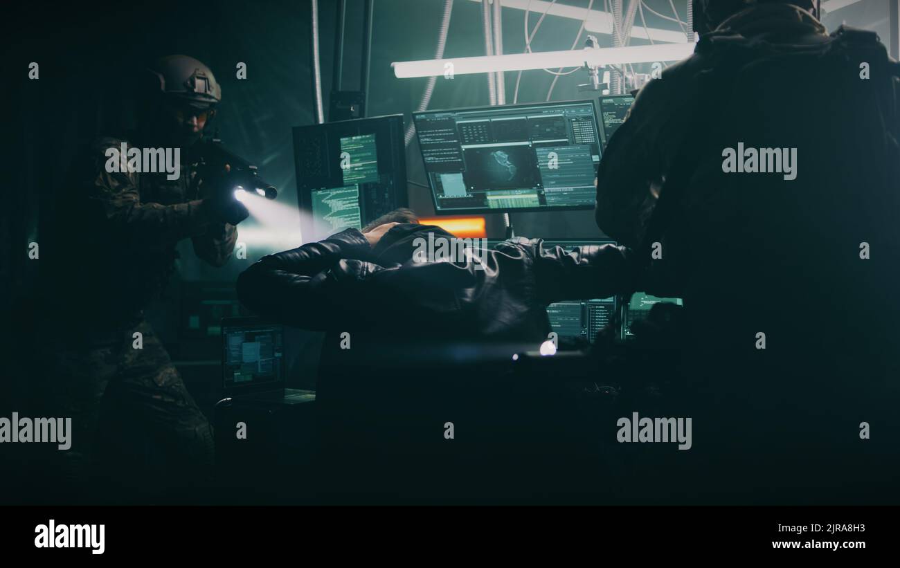 Polizei taktische Einheit Soldaten mit Gewehren Verhaftungen Cyber-Kriminelle während Hacker-Angriff auf Datenbank in dunklen Raum mit modernen Computern Stockfoto