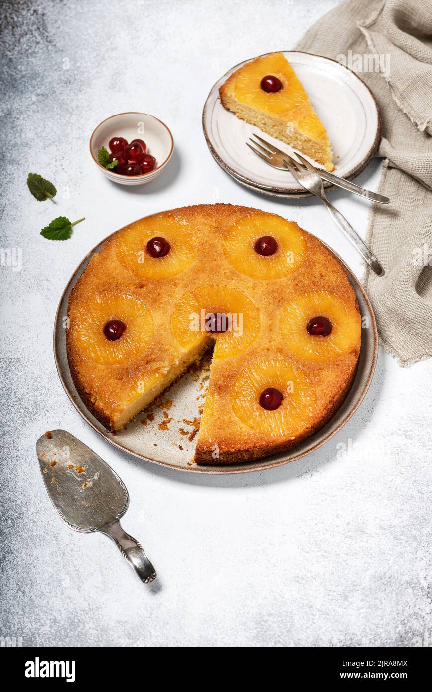 Hausgemachter Ananaskuchen auf dem Kopf mit kandierten Kirschen und einem Stück auf einem Teller abgeschnitten. Tropisches Dessert im Sommer. Selektiver Fokus. Stockfoto