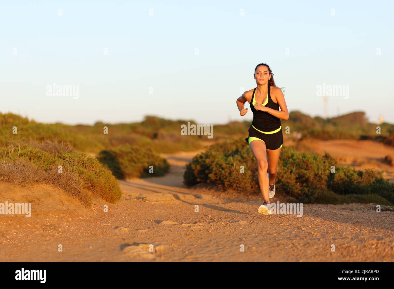 Läuferin, die bei Sonnenuntergang in den Bergen auf die Kamera zuläuft Stockfoto
