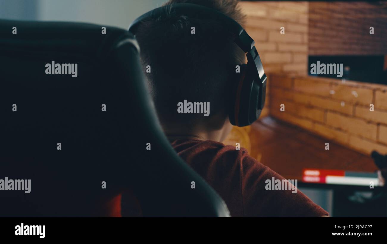 Tracking-Aufnahme eines anonymen Teenie-Spielers, der am Ende des Spiels während des Cybersport-Wettbewerbs das Headset auszieht, während er zu Hause am Tisch sitzt Stockfoto