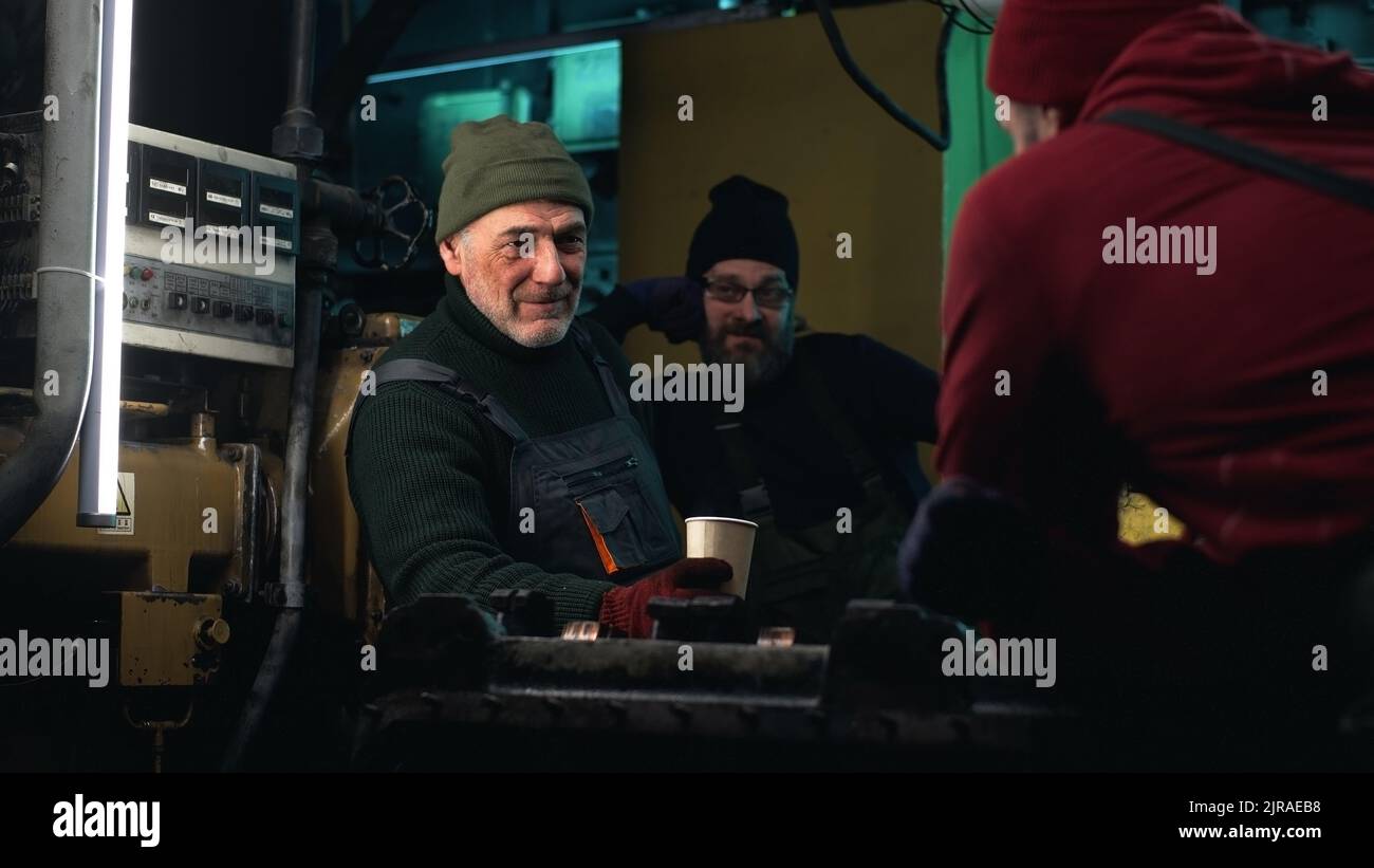 Zoom in der Ansicht eines älteren Mannes mit Getränk, der während der Pause mit Kollegen über die Arbeit auf dem Fischerboot diskutiert Stockfoto