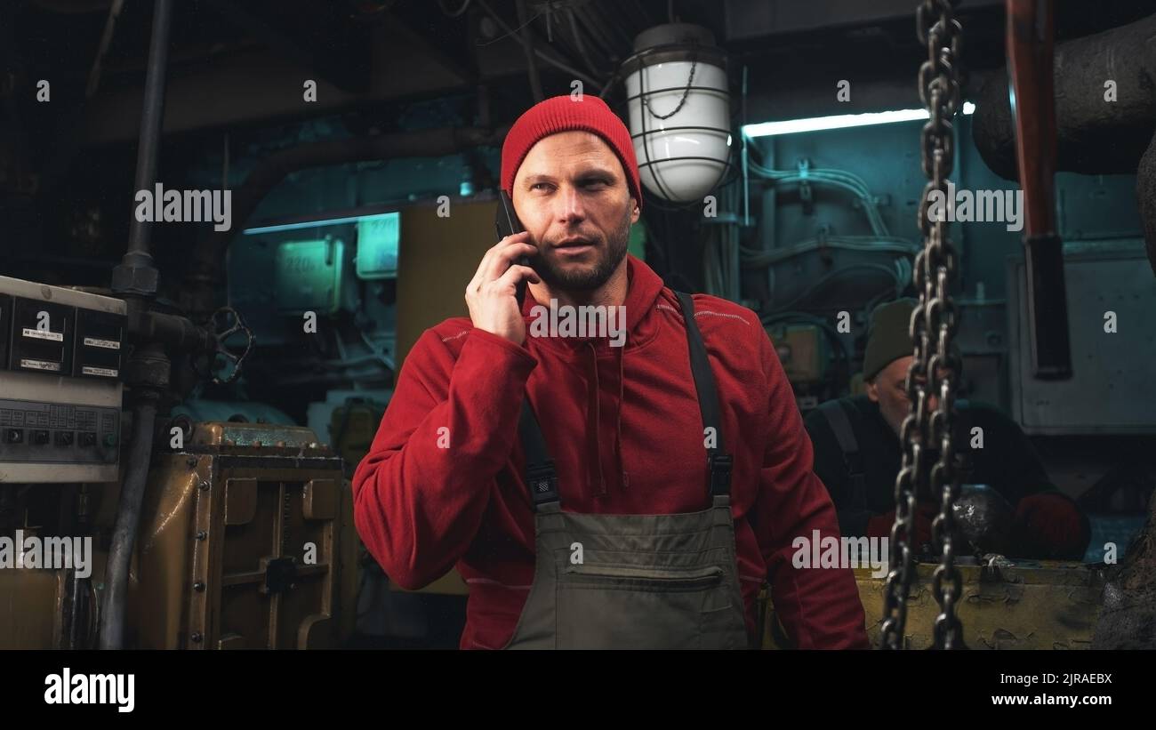 Zoomen Sie in der Ansicht eines männlichen Ingenieurs, der während der Reparatur eines Schiffsmotors in der Nähe von Kollegen telefoniert Stockfoto