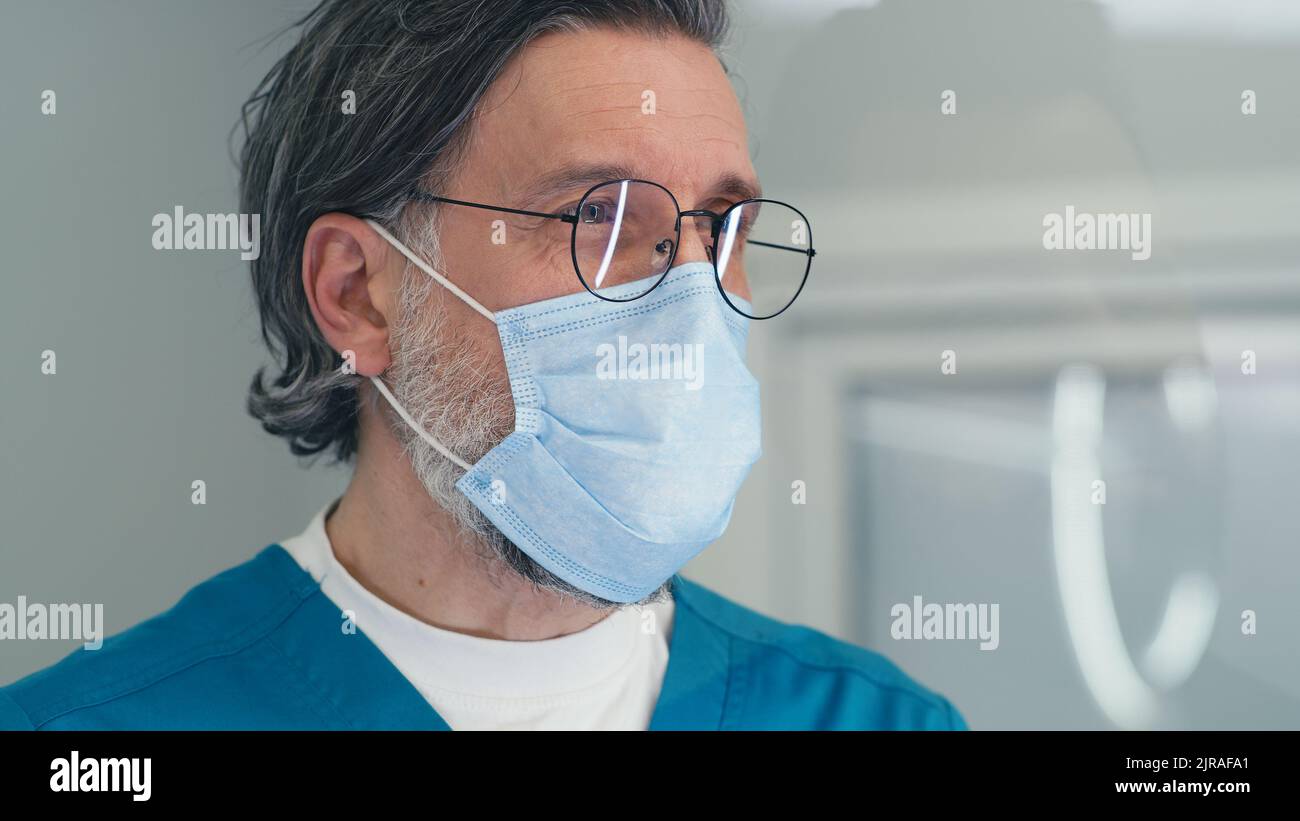 Arzt mittleren Alters, der hinter Glas steht und mit dem Patienten spricht, während er an der Aufnahme der Klinik während der Epidemie arbeitet Stockfoto