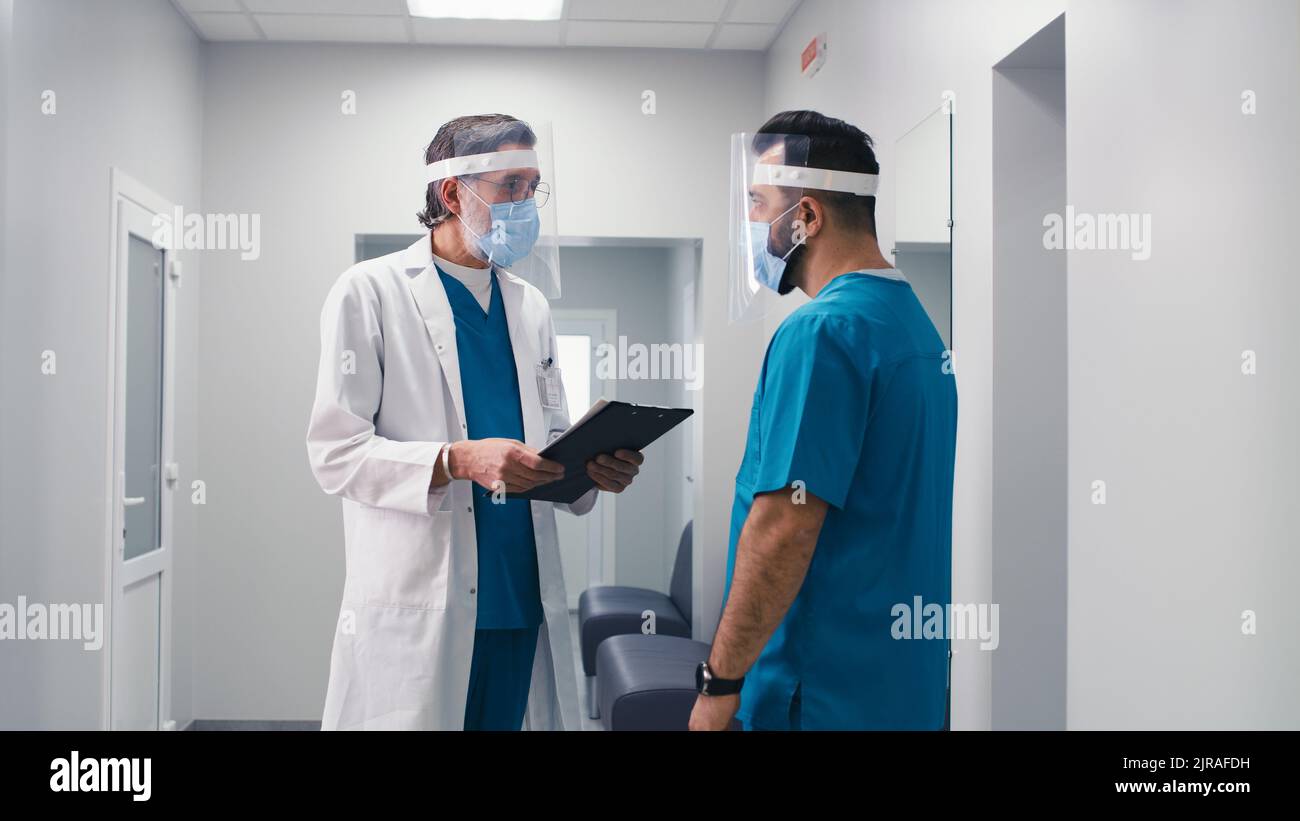 Asiatische Frau in medizinischer Uniform und Gesichtsschutz laufen und rufen Kollegen während der Notfall in der modernen Klinik Stockfoto