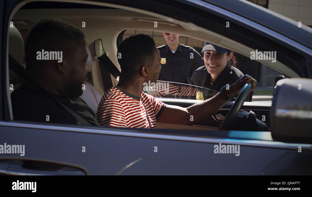 Positive Frau in Polizeiuniform im Gespräch mit afroamerikanischem Mann im Auto und Scannen digitalen Führerschein auf dem Smartphone Stockfoto