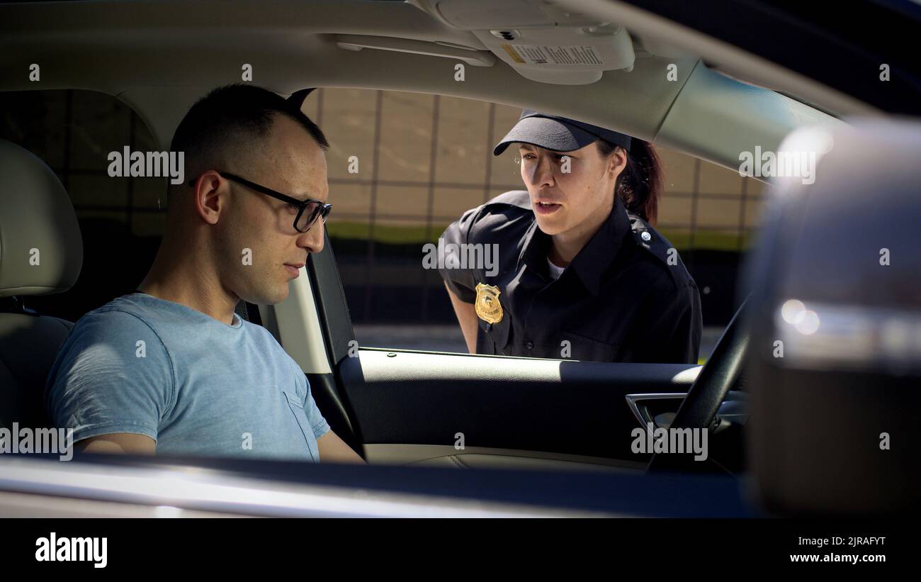 Seriöse Frau in Polizeiuniform, die den Führerschein überprüft und dem Mann, der im Auto auf der Stadtstraße sitzt, Fragen stellt Stockfoto