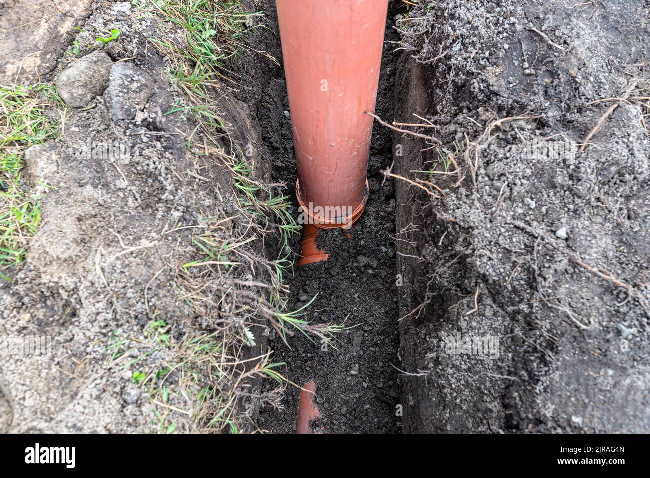 Ein orangefarbenes Kunststoffrohr aus einem Klärbecken mit einem Durchmesser von 160 mm, das in einem Graben liegt, sichtbares Rohr zur Revision. Stockfoto