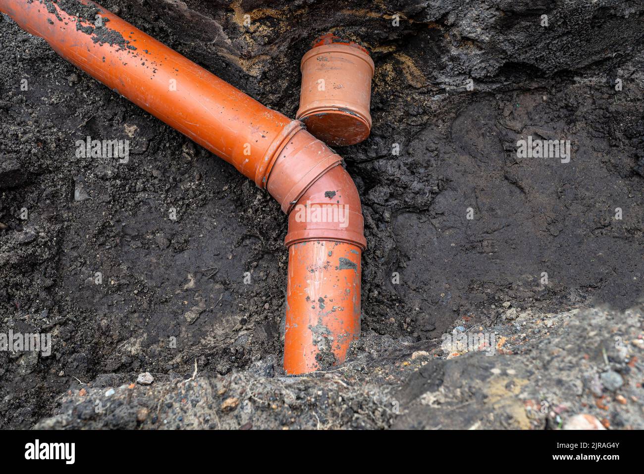 Ein orangefarbenes Kunststoffrohr aus einem Klärbecken mit einem Durchmesser von 160 mm, das in einem Graben liegt, ein blindes Rohr ist sichtbar. Stockfoto