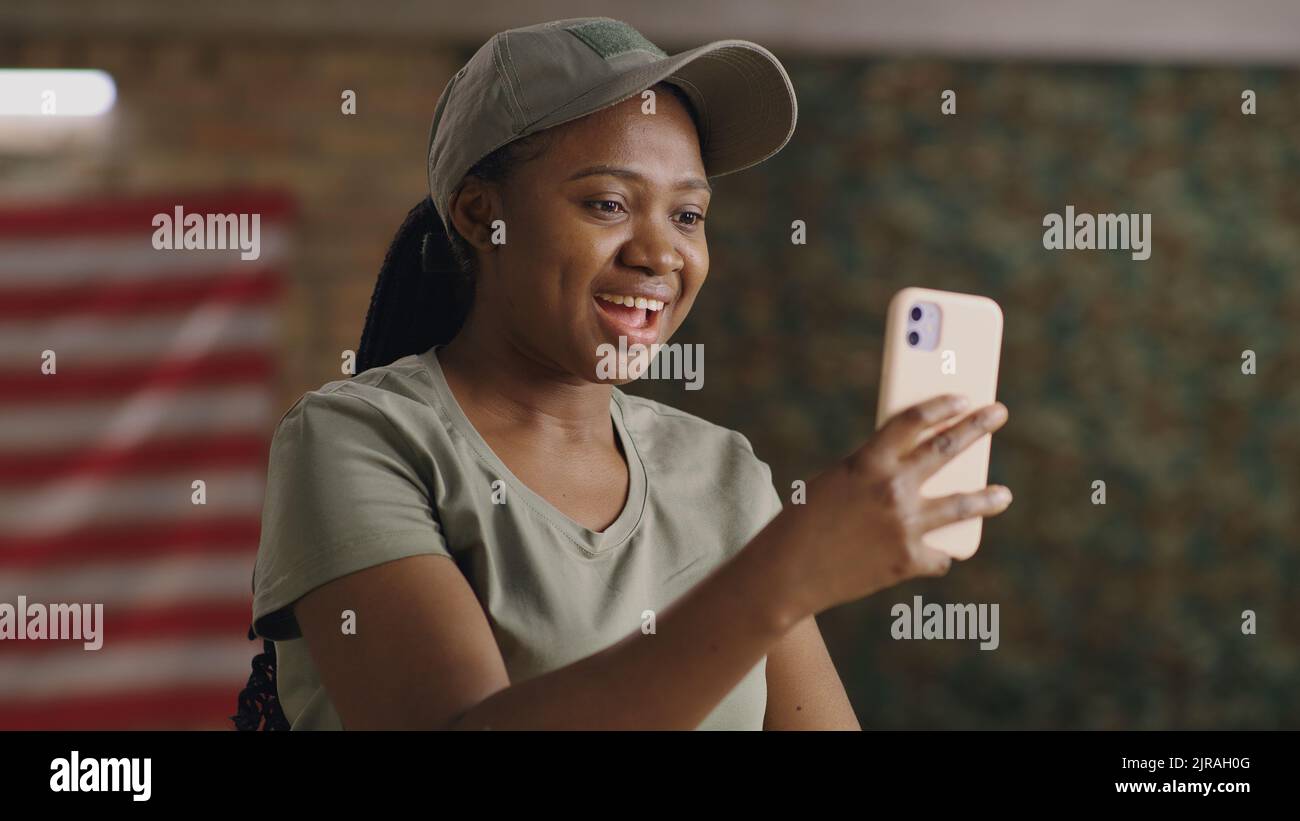 Glückliche schwarze Frau lächelt und winkende Hand, während sie mit dem Smartphone mit einem Online-Freund auf dem Militärstützpunkt der USA spricht Stockfoto