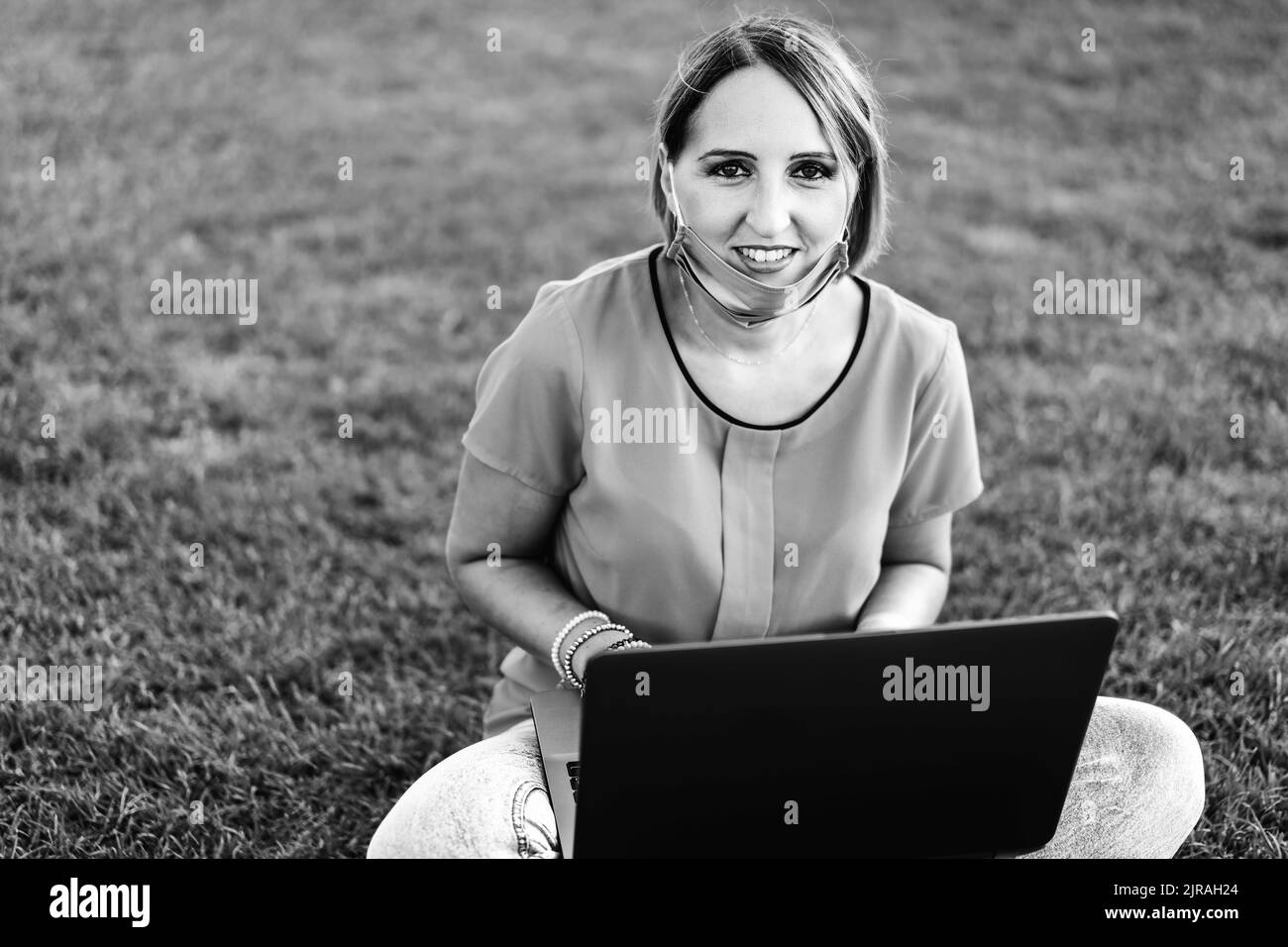 Frau 40 Jahre alt arbeitet im Freien mit Laptop während Coronavirus Outbreak - lächelnde weibliche Unternehmer sitzen auf Rasen mit persönlichen Während des Computers Stockfoto
