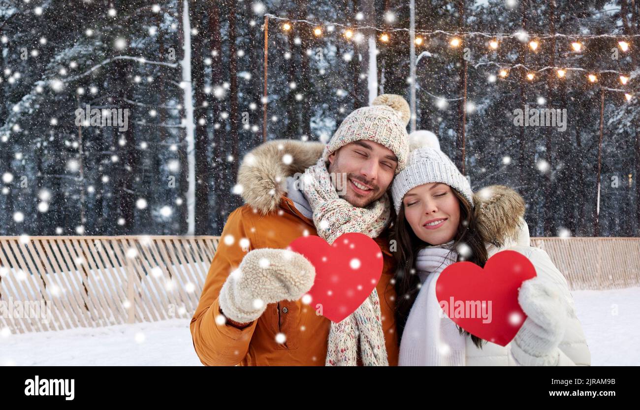 Glückliches Paar mit roten Herzen auf der Eisbahn im Winter Stockfoto