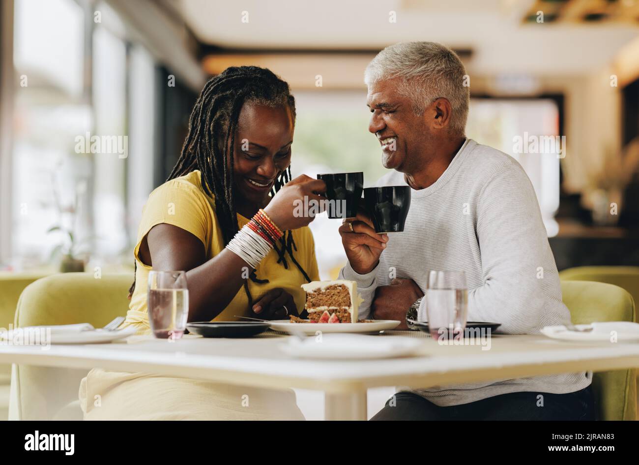Ein älteres Paar lacht fröhlich, während es in einem Café zusammen isst. Glückliches Seniorenpaar, das eine gute Zeit in einem Restaurant hatte. Reifes Paar enjoyi Stockfoto
