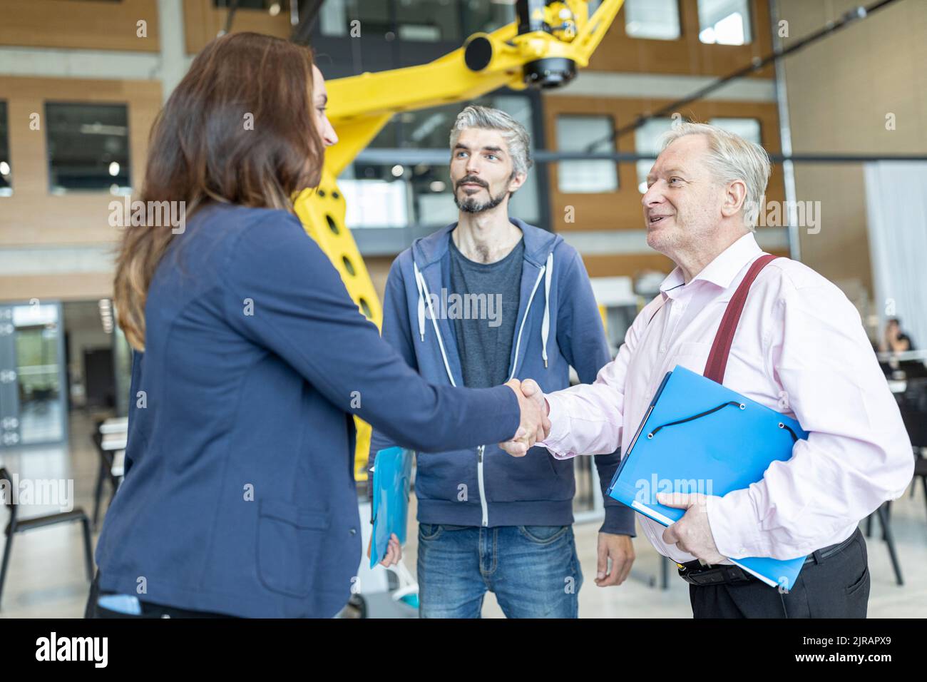 Leitende Technikerin schüttelt sich die Hände mit einer Kollegin in der Fabrik mit Industrierobotern Stockfoto