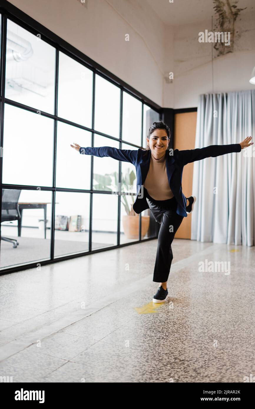 Sorglose junge Geschäftsfrau, die auf einem Bein im Büro steht Stockfoto