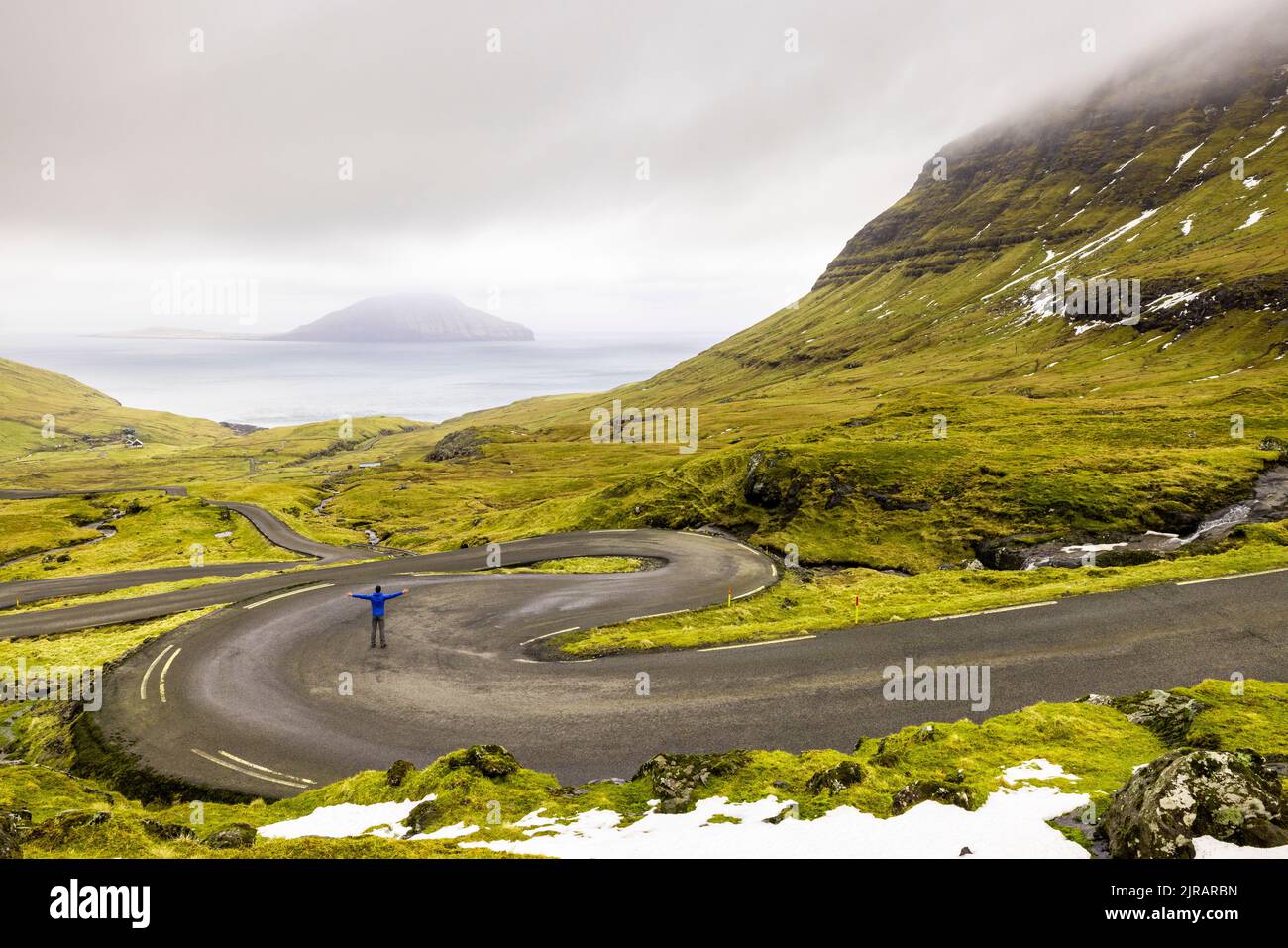 Färöer-Inseln, Streymoy, Mann, der mitten auf einer abgelegenen, kurvenreichen Straße steht Stockfoto
