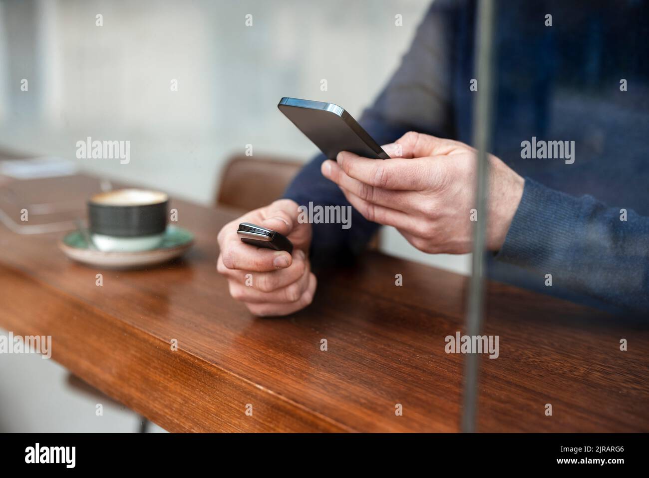 Hände eines Geschäftsmannes, der den Autoschlüssel mit dem Smartphone im Café hält, das durch das Glasfenster gesehen wird Stockfoto