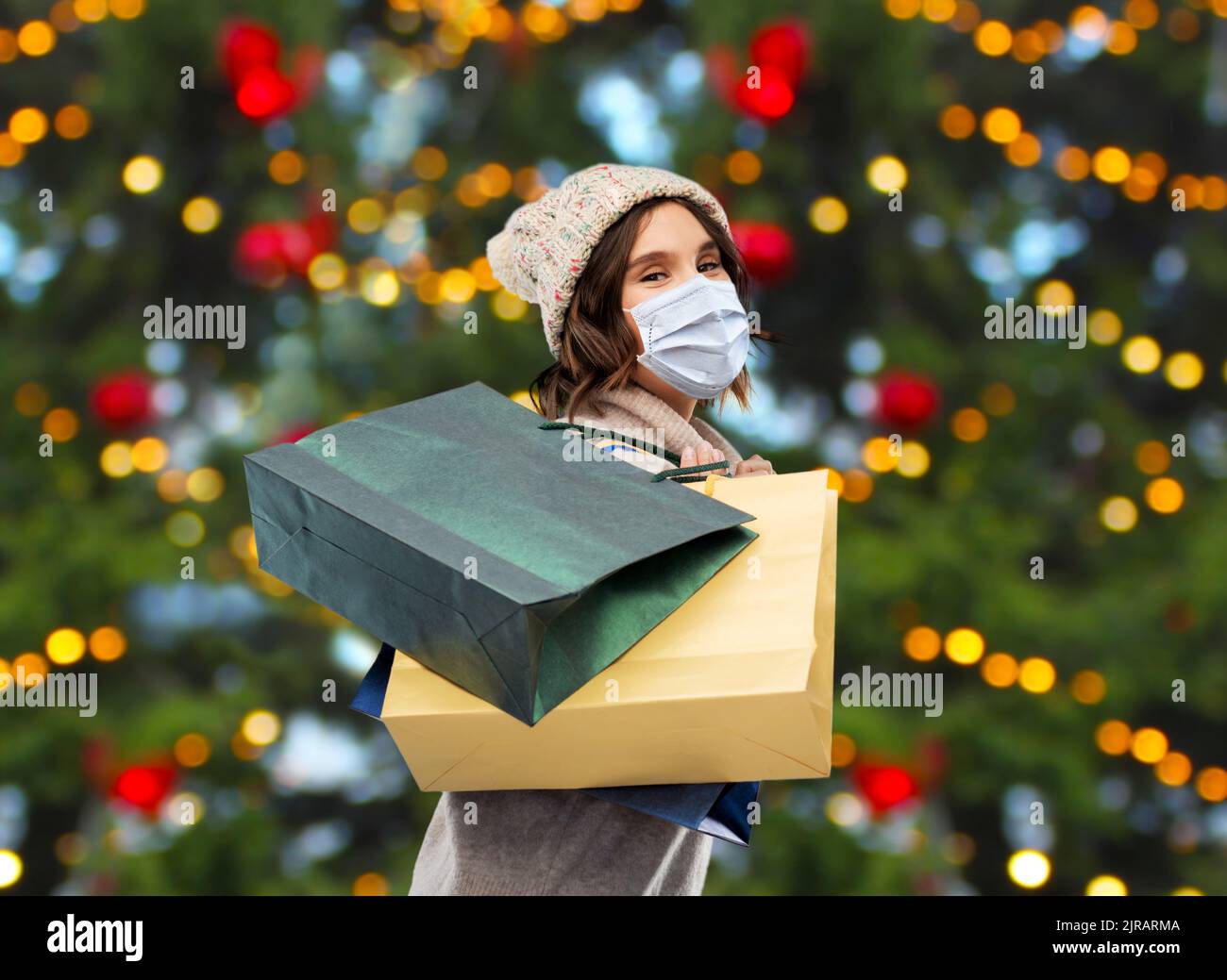 Frau in Gesichtsmaske mit Einkaufstaschen zu weihnachten Stockfoto