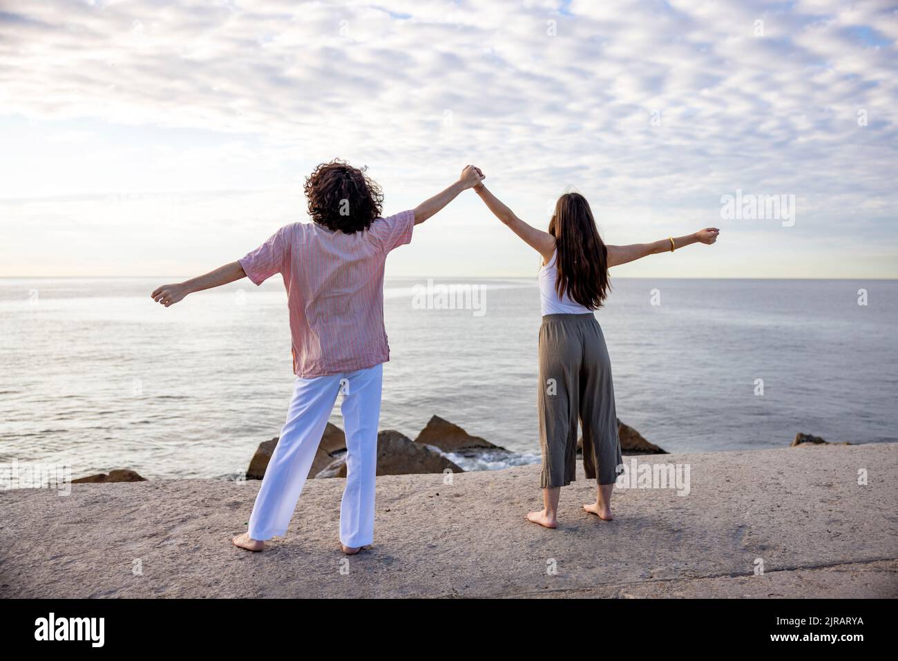 Paar hält die Hände mit ausgestreckten Armen auf dem Pier und blickt auf das Meer Stockfoto