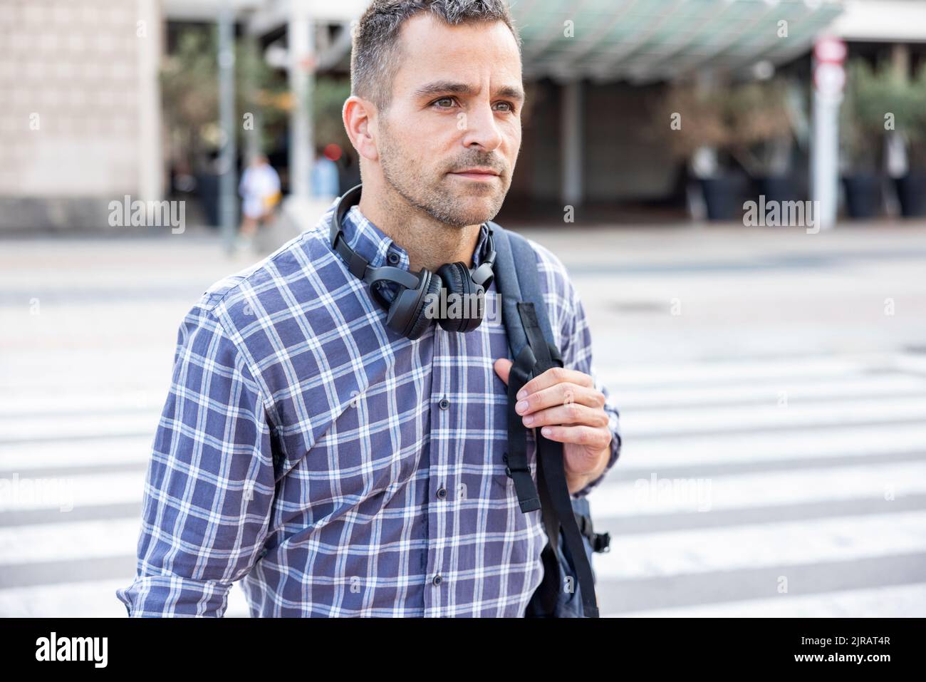 Reifer Mann mit kabellosen Kopfhörern und Rucksack über die Straße Stockfoto