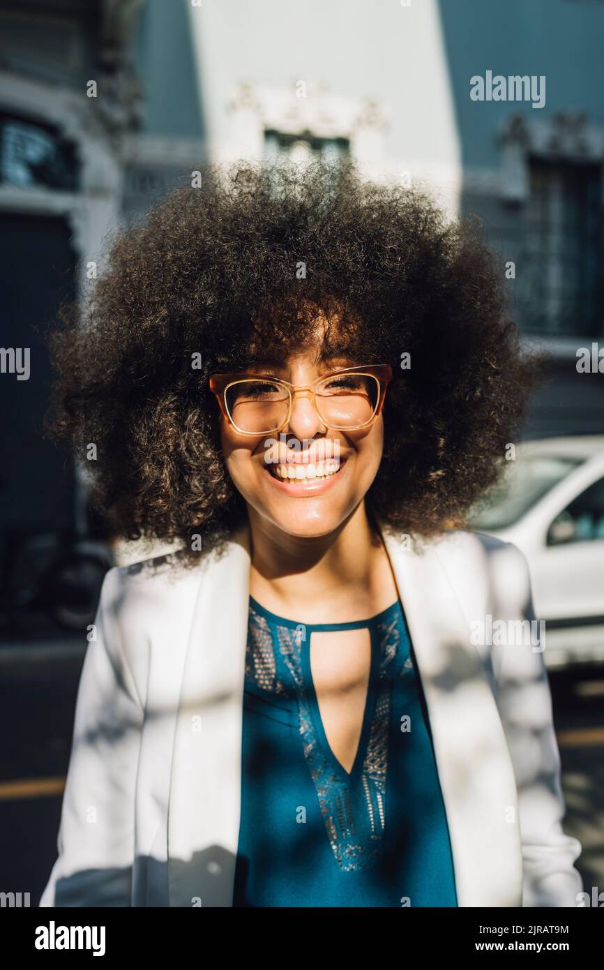 Glückliche Geschäftsfrau mit Afro-Frisur, die an sonnigen Tagen eine Brille trägt Stockfoto