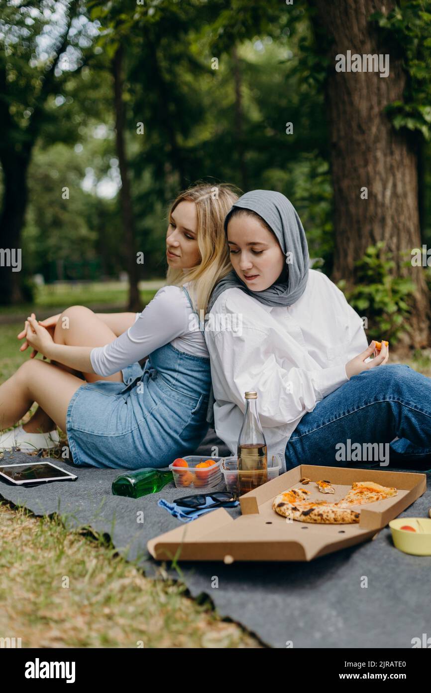 Junge Freunde, die sich auf einer Picknickdecke mit Essen und Trinken im Park zurücklehnen Stockfoto