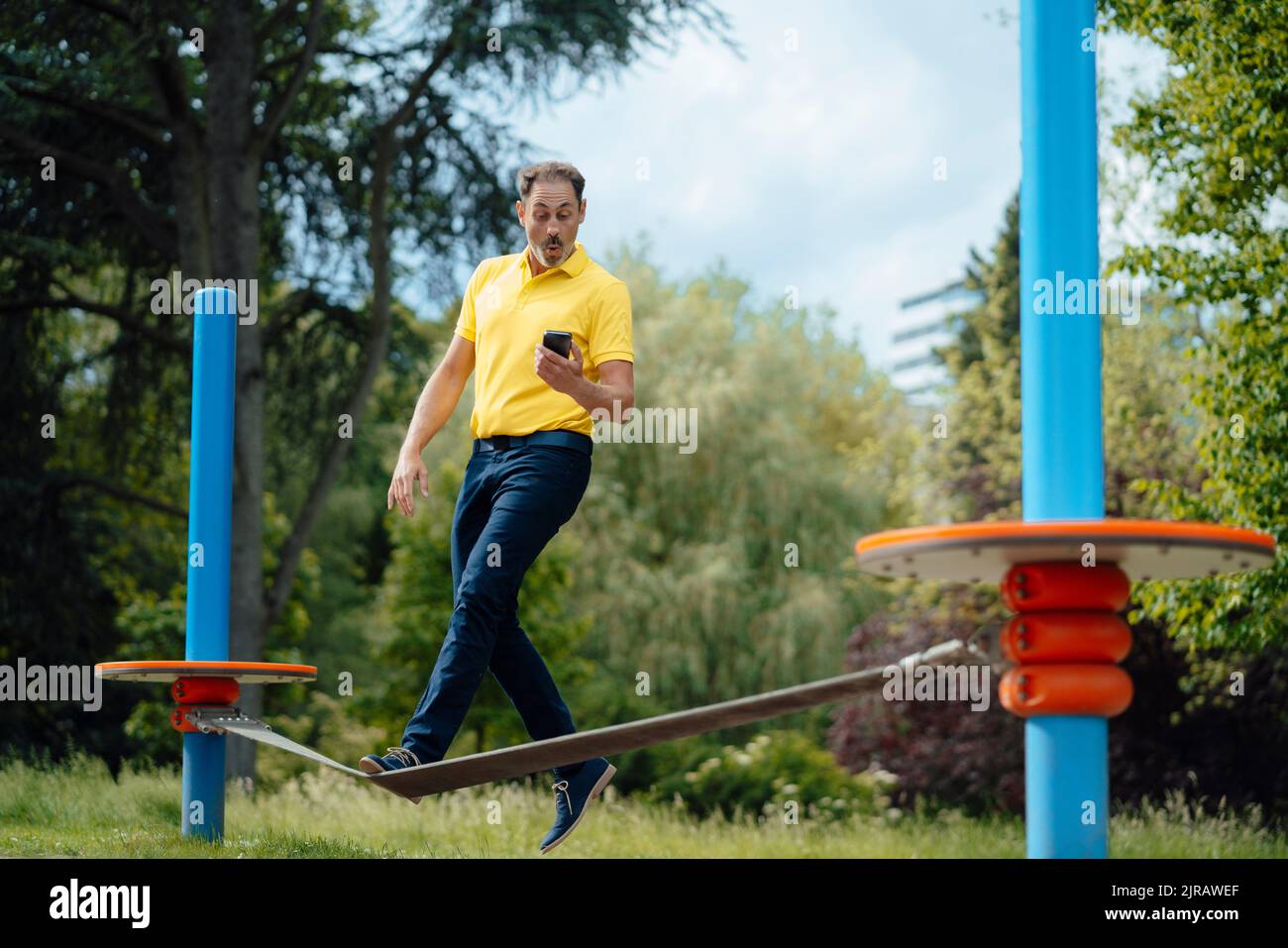 Überraschender Mann, der Smartphone beim Gratwanderung im Park betrachtet Stockfoto