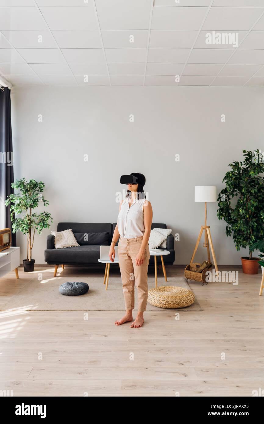 Frau trägt Virtual-Reality-Simulator Brille im Wohnzimmer stehen Stockfoto