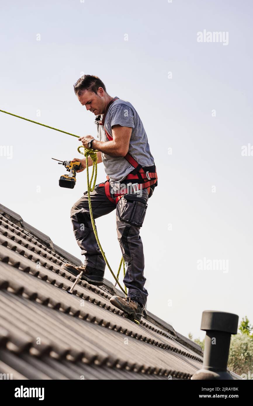 Handwerker mit Elektrowerkzeug, das Seil auf dem Dach hält Stockfoto