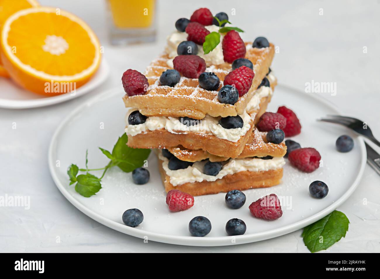 Frische Wiener oder belgische Waffeln auf einem Teller mit frischen Himbeeren und Blaubeeren und Schlagsahne. Stockfoto